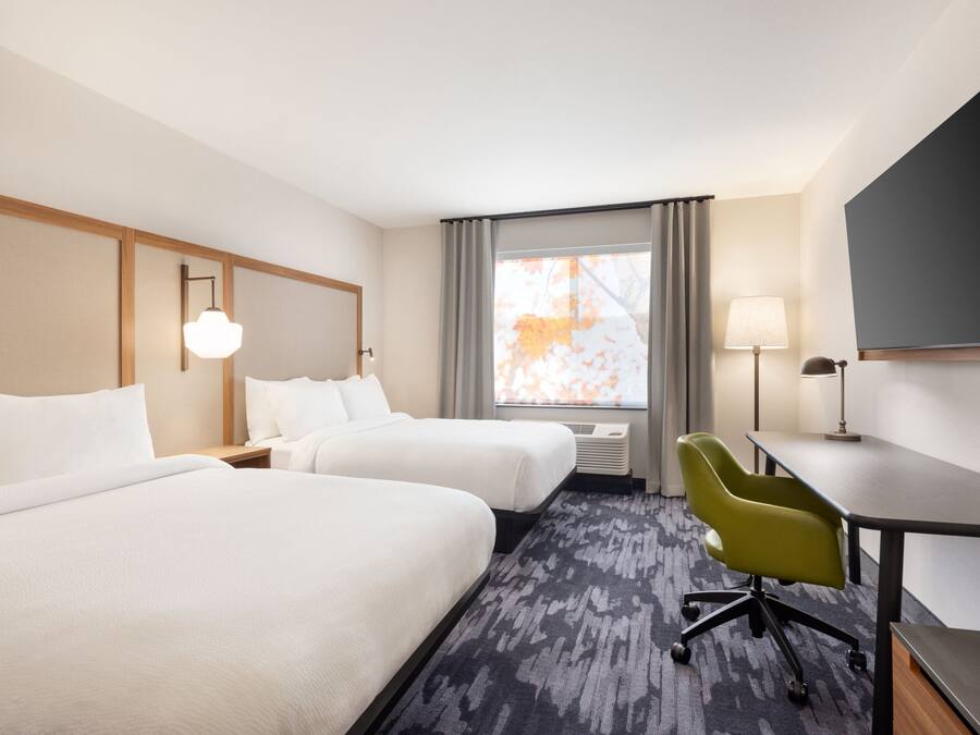 A hotel room with two beds, a desk, a chair, a TV, and a window with curtains.