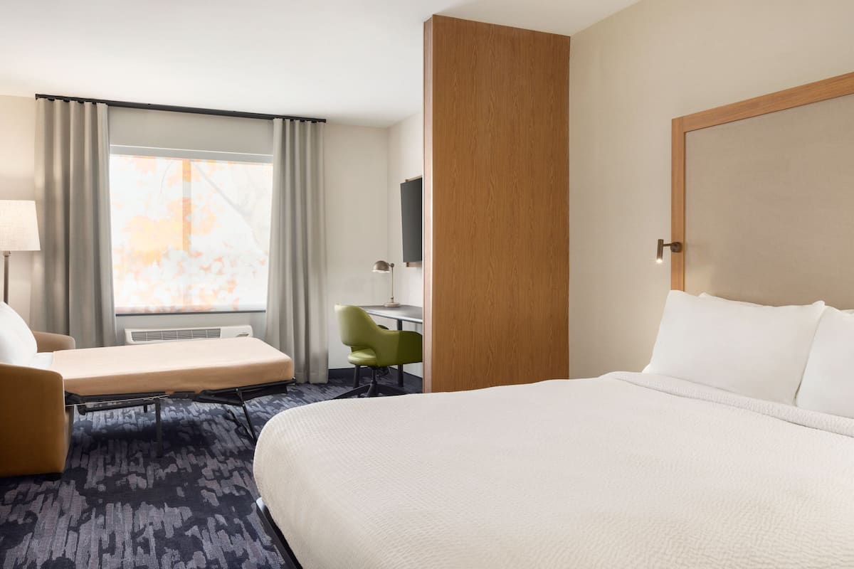 A hotel room with a large bed, a desk, a chair, and a window with curtains.