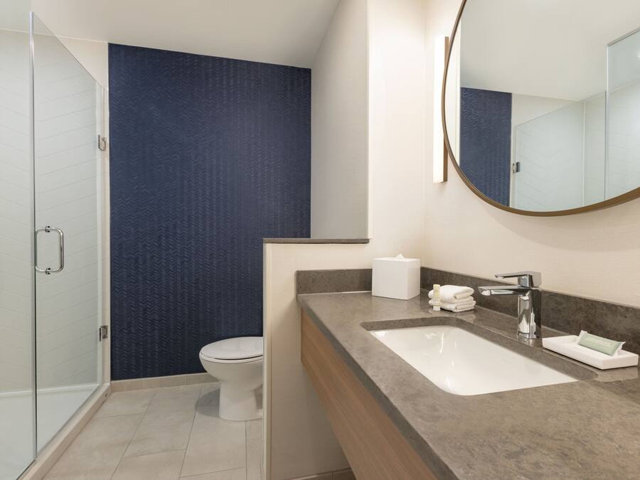 Un baño moderno con cabina de ducha de vidrio, inodoro blanco y lavamanos de mármol con espejo.