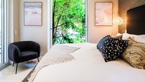 Un dormitorio con una cama, una silla y una puerta que da a un área verde al aire libre.