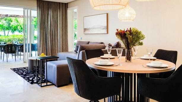 Un comedor moderno con una mesa redonda, sillas negras y un florero con flores.