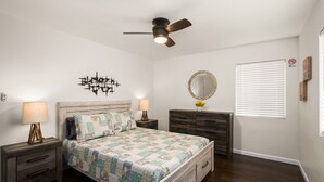 A bedroom with a bed, nightstands, a dresser, a ceiling fan, a mirror, and a window with blinds.