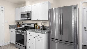 A modern kitchen with white cabinets, a stainless steel refrigerator, a microwave, and a gas stove.