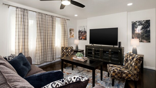 A living room with a sofa, armchair, coffee table, TV, and a ceiling fan.