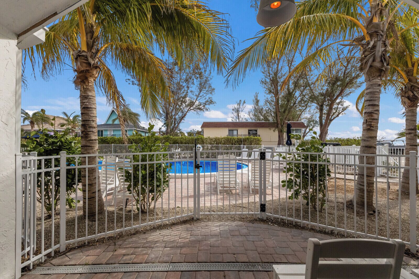 Un patio cubierto con piscina, palmeras y cerca blanca.