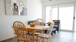 Un coin repas avec une table et des chaises en bois, un saladier rempli de fruits et un tableau accroché au mur.