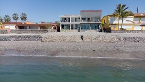 Un bâtiment situé sur la côte, doté d’un mur en pierre, d’un balcon et offrant une vue dégagée sur la plage.