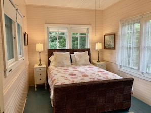 A bedroom with a large bed, two bedside tables, a window with a view of greenery, and a framed picture on the wall. - Arts & Crafts Cottage In Picturesque Bayside, Maine (Northport)