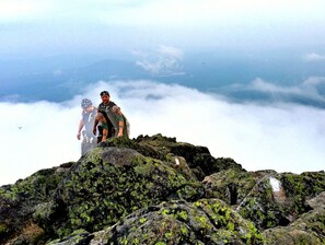 A rocky mountain peak with two people standing on it, surrounded by clouds. - Arts & Crafts Cottage In Picturesque Bayside, Maine (Northport)