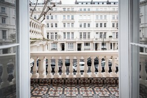 A view from a balcony with a tiled floor, a white balustrade, and a row of parked cars in the background. - MSK Premium (London)