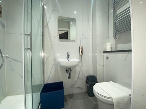 A modern bathroom with a glass shower enclosure, a white sink, and a toilet. - MSK Premium (London)