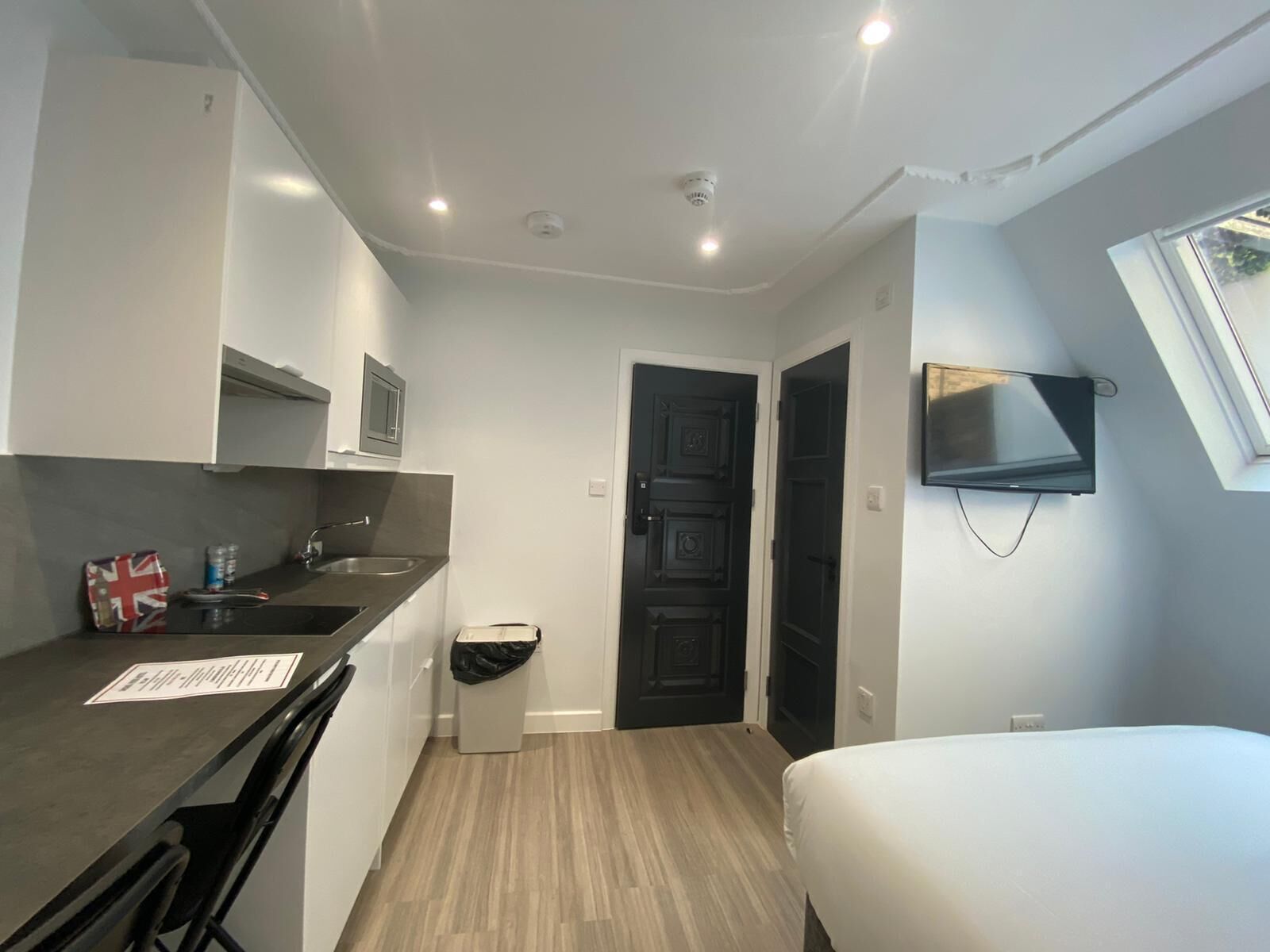 Camera d'albergo compatta con angolo cottura, un letto, una TV a parete e un piccolo cestino.