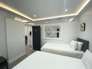 A modern bedroom with two beds, a window, and a door. - MSK Premium (London)