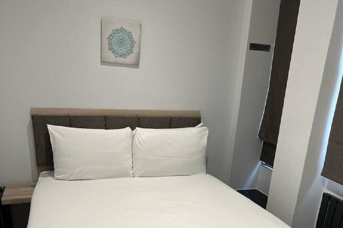 A neatly made bed with white linens in a modern room with a wooden headboard and a small decorative item on the wall.