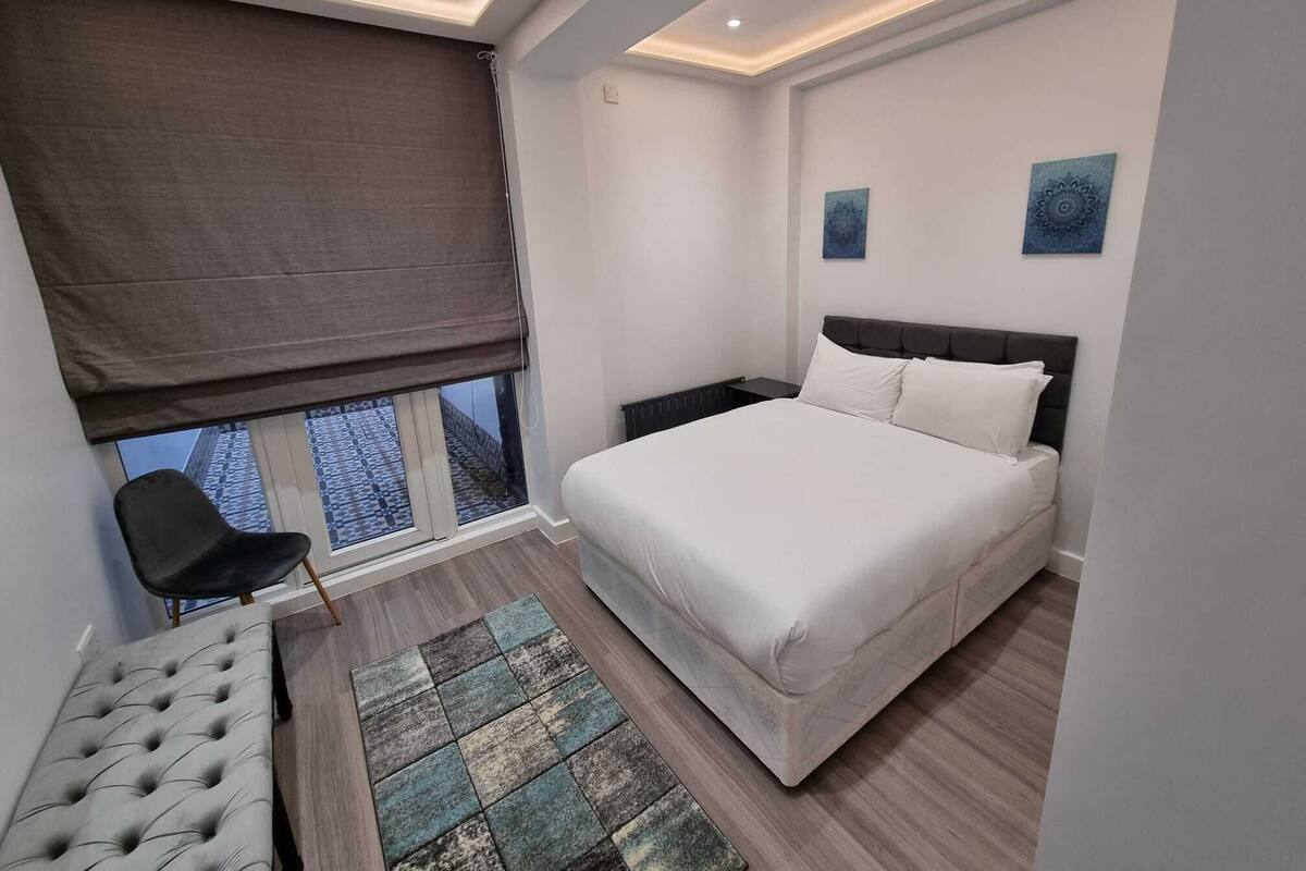 A modern bedroom with a large bed, a chair, a window with a view, and two wall art pieces.