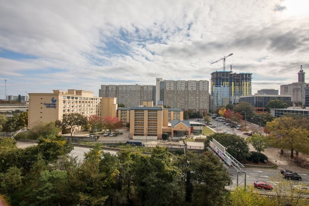 A cityscape with a mix of residential and commercial buildings, including a prominent university building with a crane on a nearby construction site.