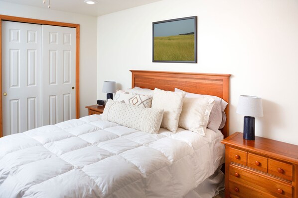 A neatly made bed with a white duvet, a wooden headboard, and a nightstand with a lamp.