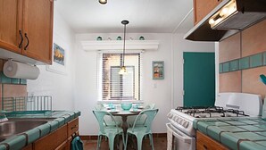 Una cocina compacta con armarios de madera, estufa a gas, lavamanos y una mesa de comedor con sillas.