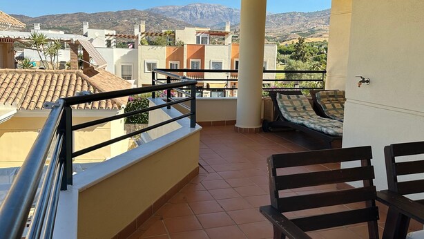 Ein Balkon mit Fliesenboden, Geländer und Blick auf eine gebirgige Landschaft.