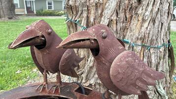 Two rusted metal bird sculptures mounted on a metal structure, with a tree and a house in the background.
