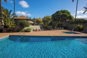 A clear blue pool with a ladder, surrounded by lounge chairs and palm trees, with buildings in the background. - Kihei Bay Surf 227 by Maui Rental Group (Kihei)
