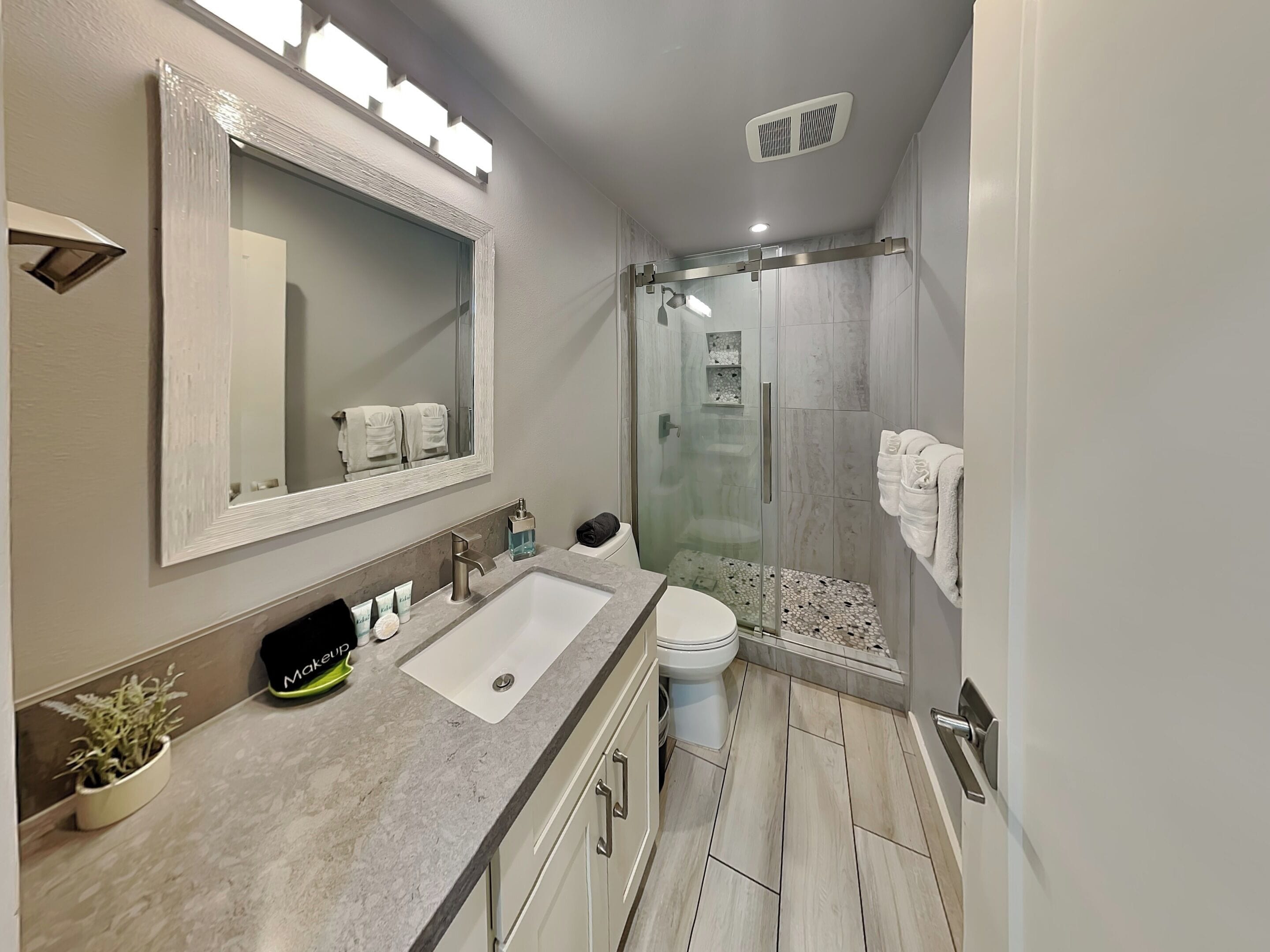 A modern bathroom with a large mirror, a sink, a toilet, and a shower area.