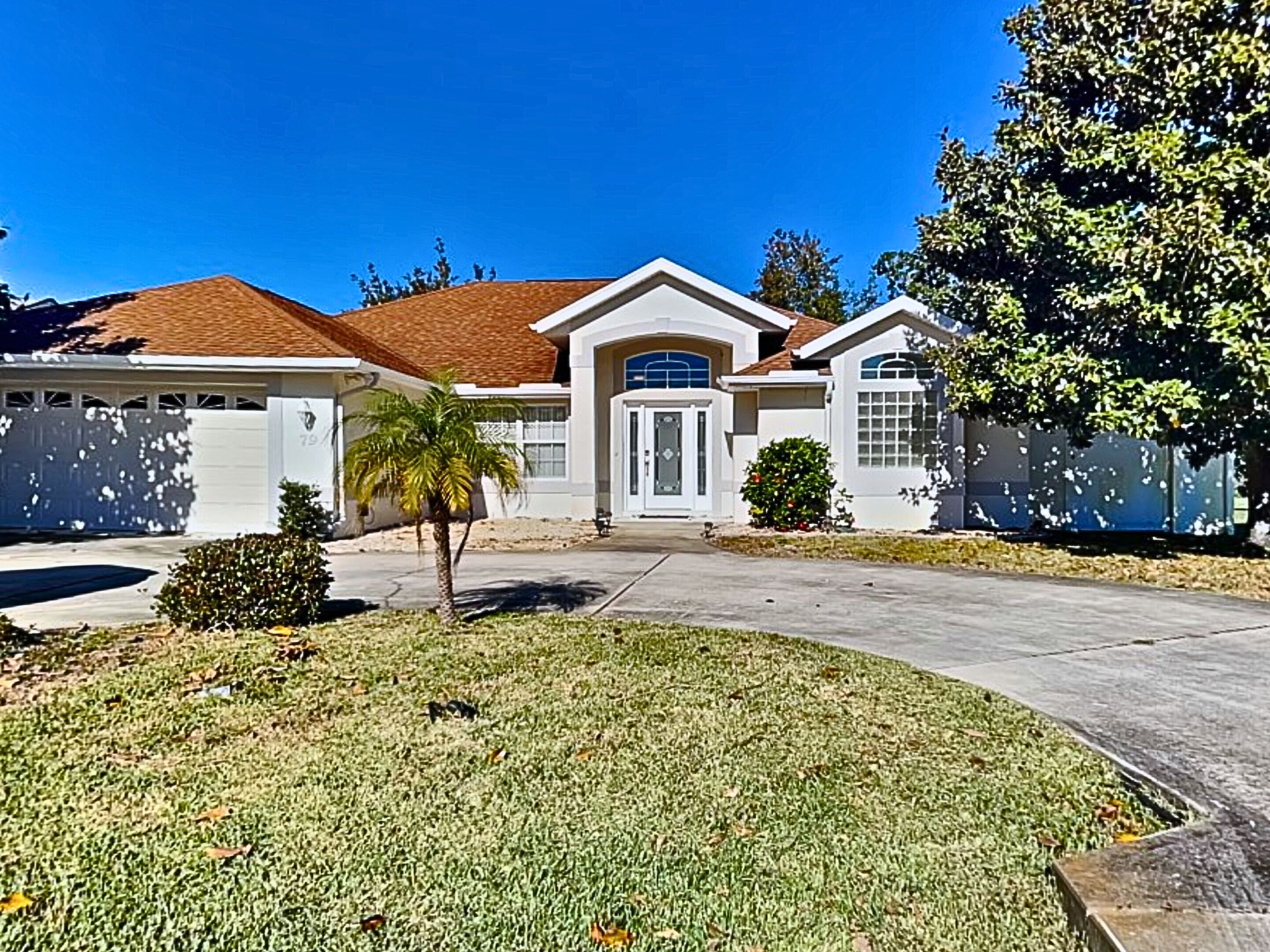 A residential house with a garage, a front door, and a small lawn with a palm tree.