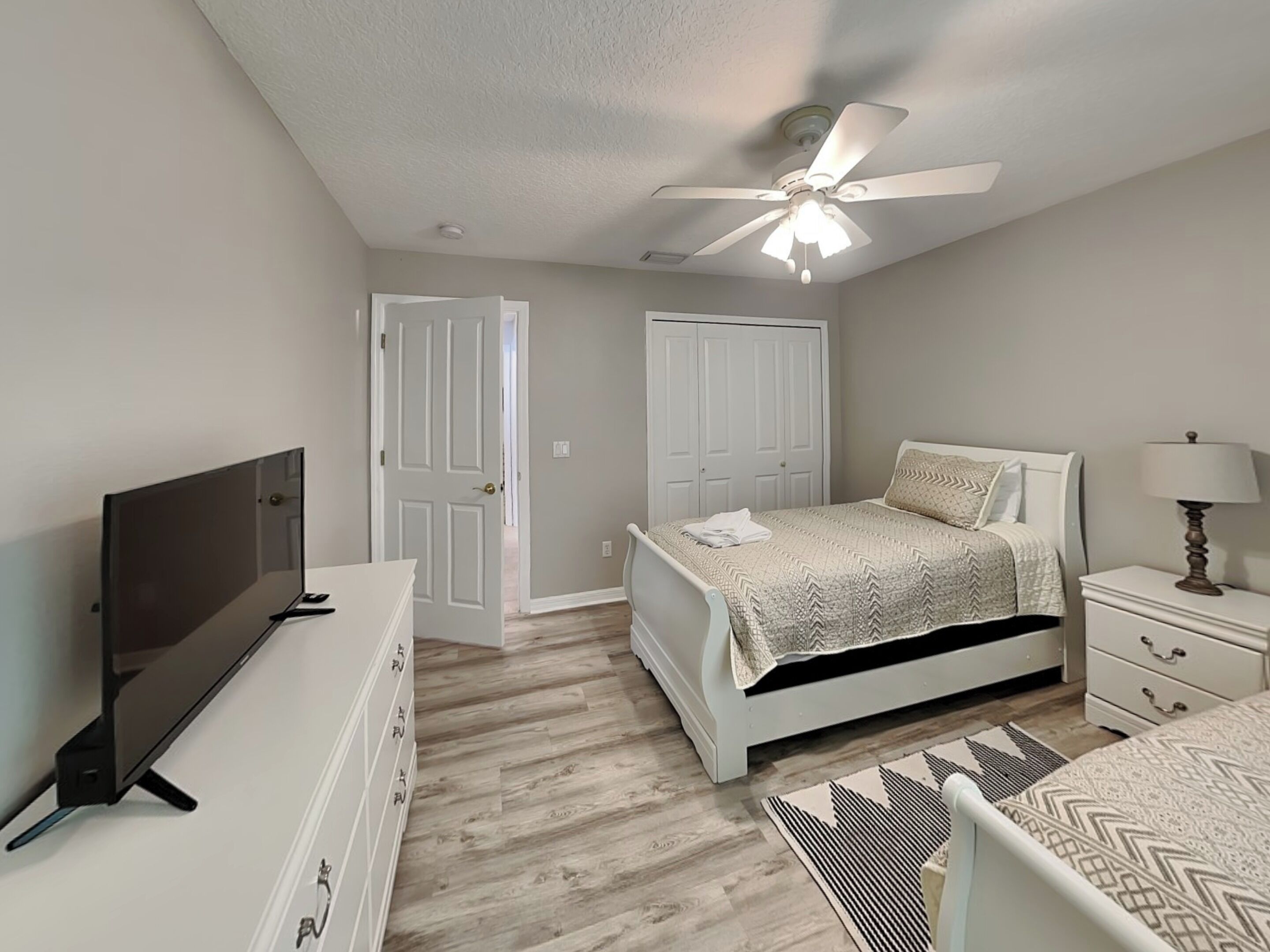 A bedroom with a bed, a TV, a ceiling fan, and a nightstand.