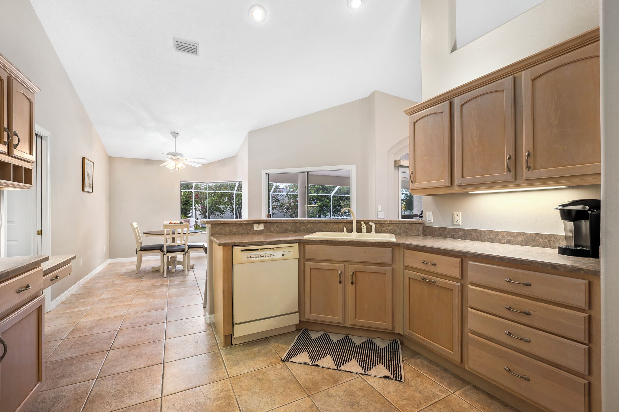 A kitchen with wooden cabinets, a dishwasher, and a dining area with chairs and a table.