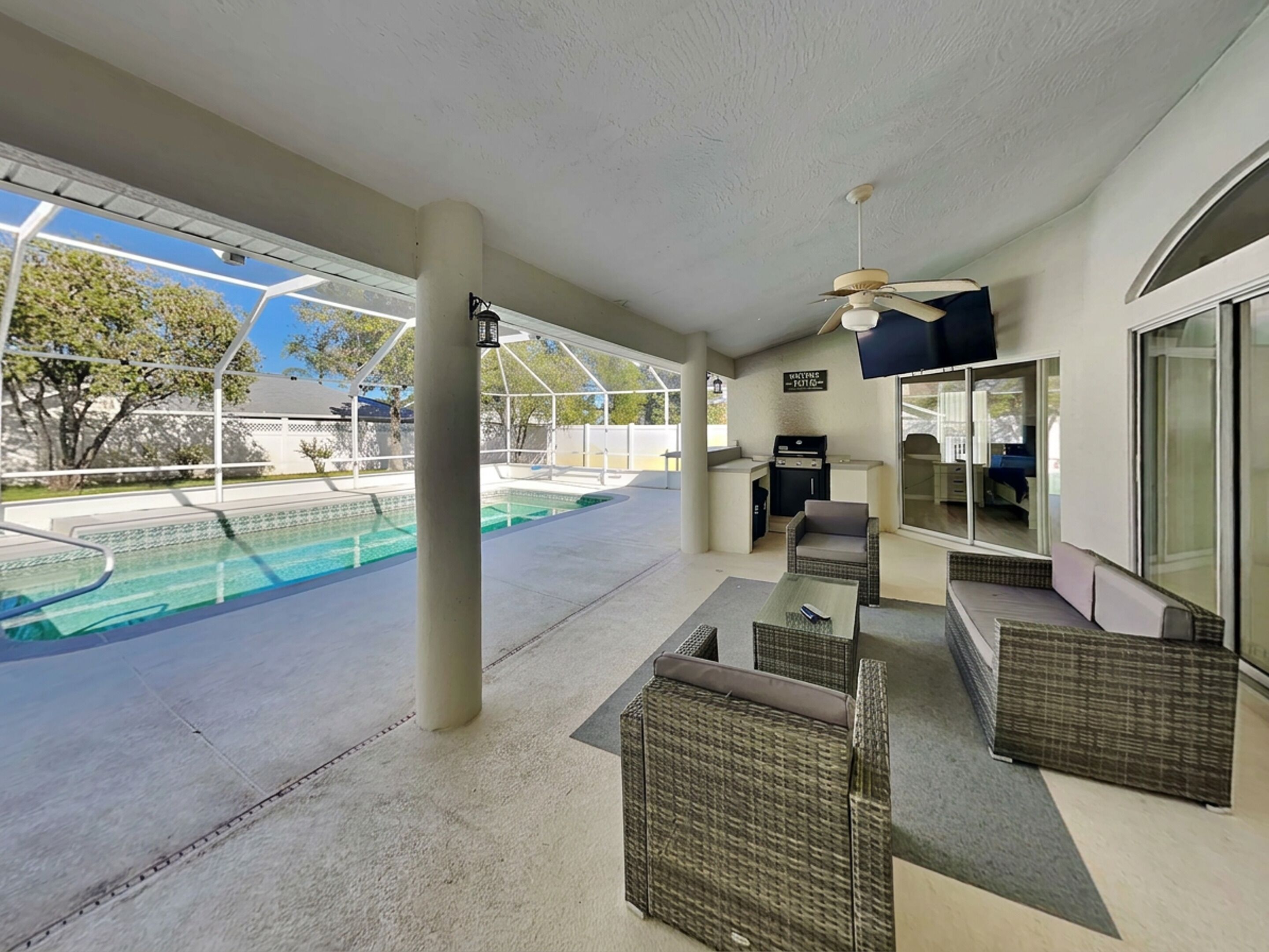 A covered outdoor area with a pool, seating, a grill, and a ceiling fan.