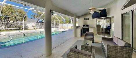 A covered outdoor area with a pool, seating, a grill, and a ceiling fan.