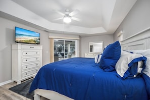 Een slaapkamer met een bed, een dressoir, een televisie en een plafondventilator.