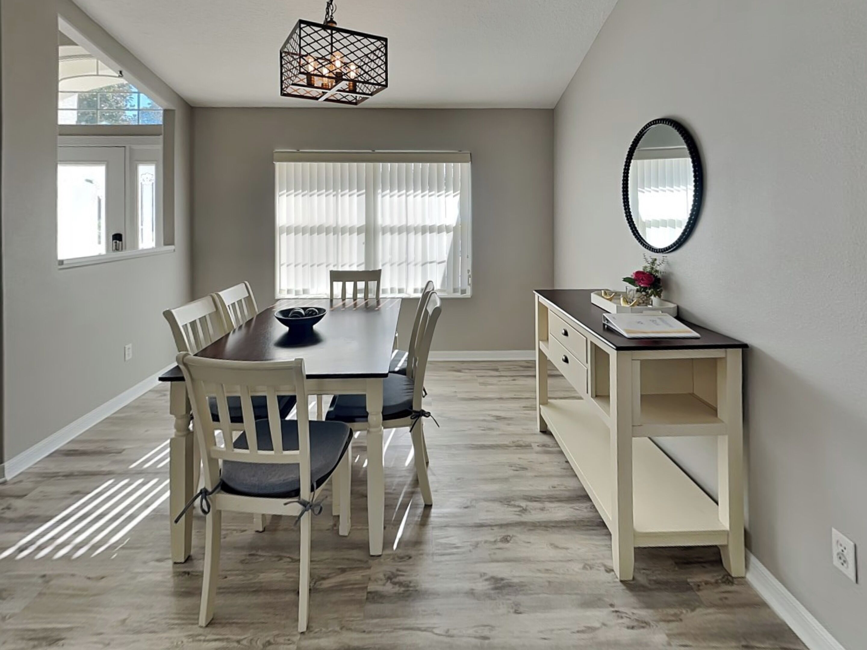 A dining area with a wooden table, white chairs, a hanging light fixture, and a mirror on the wall.