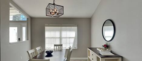 A dining area with a wooden table, white chairs, a hanging light fixture, and a mirror on the wall.