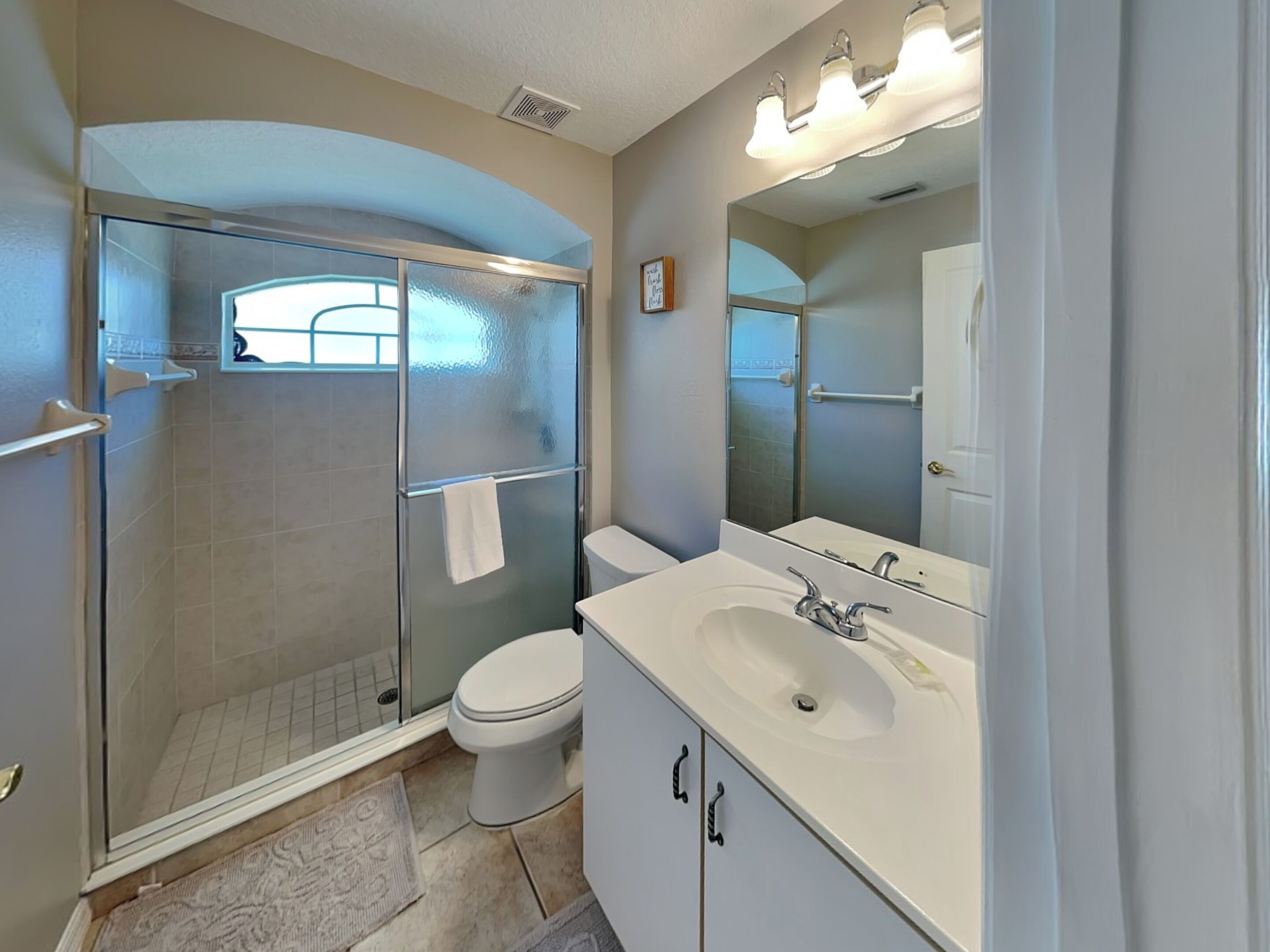 A modern bathroom with a glass-enclosed shower, a white toilet, and a vanity with a large mirror.