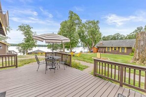 Une terrasse en bois avec une table et des chaises, un parasol à rayures et une vue sur un lac et des chalets.
