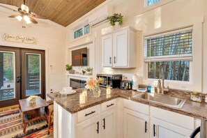 A kitchen with white cabinets, a granite countertop, a built-in microwave, and a large window with a view of trees. - Moonlight Cottage | Fire Pit and Secluded Stay (Mentone)