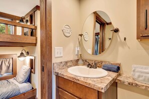 A bathroom with a wooden vanity, a round mirror, and a bed with a window view. - Black Diamond at Mentone with Free Internet! Hikes (Mentone)