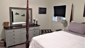 Quarto com cama de dossel, penteadeira com gavetas, espelho, janela com persiana preta e mesa de cabeceira com abajur.
