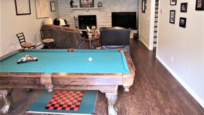 Uma sala de estar com mesa de bilhar, lareira e televisão.