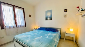 Una camera da letto con un letto, un comodino, una lampada, una finestra con tende e una parete decorata con un quadro.
