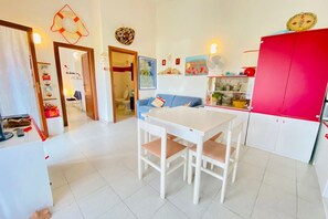 Eine Küche mit einem weißen Tisch und Stühlen, einem roten Schrank und einem blauen Sofa im Hintergrund.