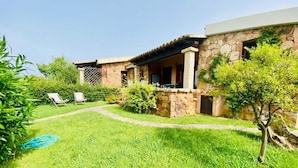 Una casa in pietra con un portico coperto, un prato e un’area giardino con un tubo da irrigazione.
