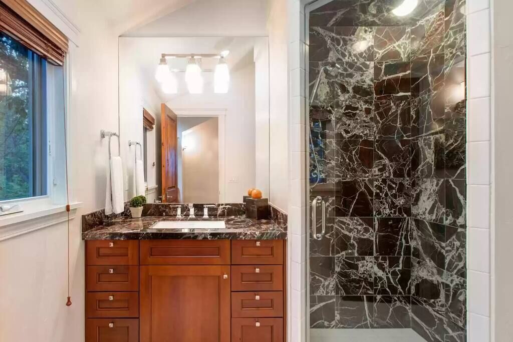 A bathroom with a marble sink, wooden cabinets, and a glass shower enclosure.