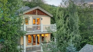 A two-story wooden cabin with a balcony on the upper floor, surrounded by dense forest. - Luxury home; king ensuites, walk to lifts/main st (Park City)