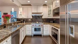 A modern kitchen with white cabinetry, a stainless steel refrigerator, a built-in oven, and a granite countertop. - Luxury home; king ensuites, walk to lifts/main st (Park City)