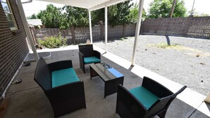 Een overdekt terras met rieten meubels en een tafel.