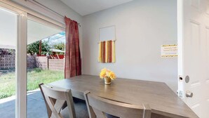 Een eetgedeelte met een houten tafel en stoelen, een vaas met gele bloemen, een schuifdeur en een bordje dat aangeeft dat dit een afzonderlijke eenheid is voor bewoning.