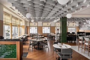 A modern restaurant with high ceilings, exposed brick walls, and a variety of seating arrangements including round tables and booths. - Hotel Forty Five, Macon, a Tribute Portfolio Hotel (Macon)