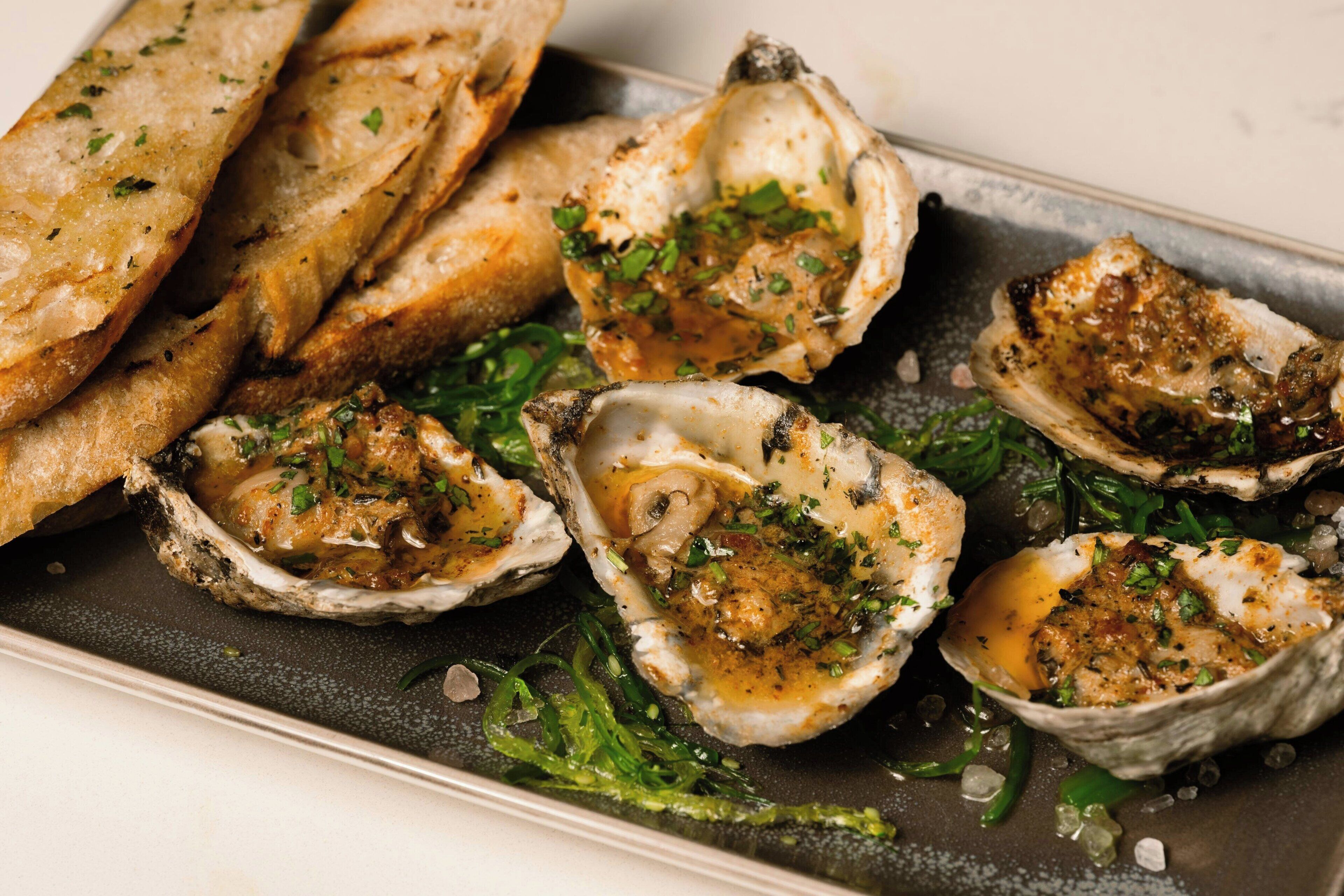 A dish of grilled oysters with herbs and a side of toasted bread.